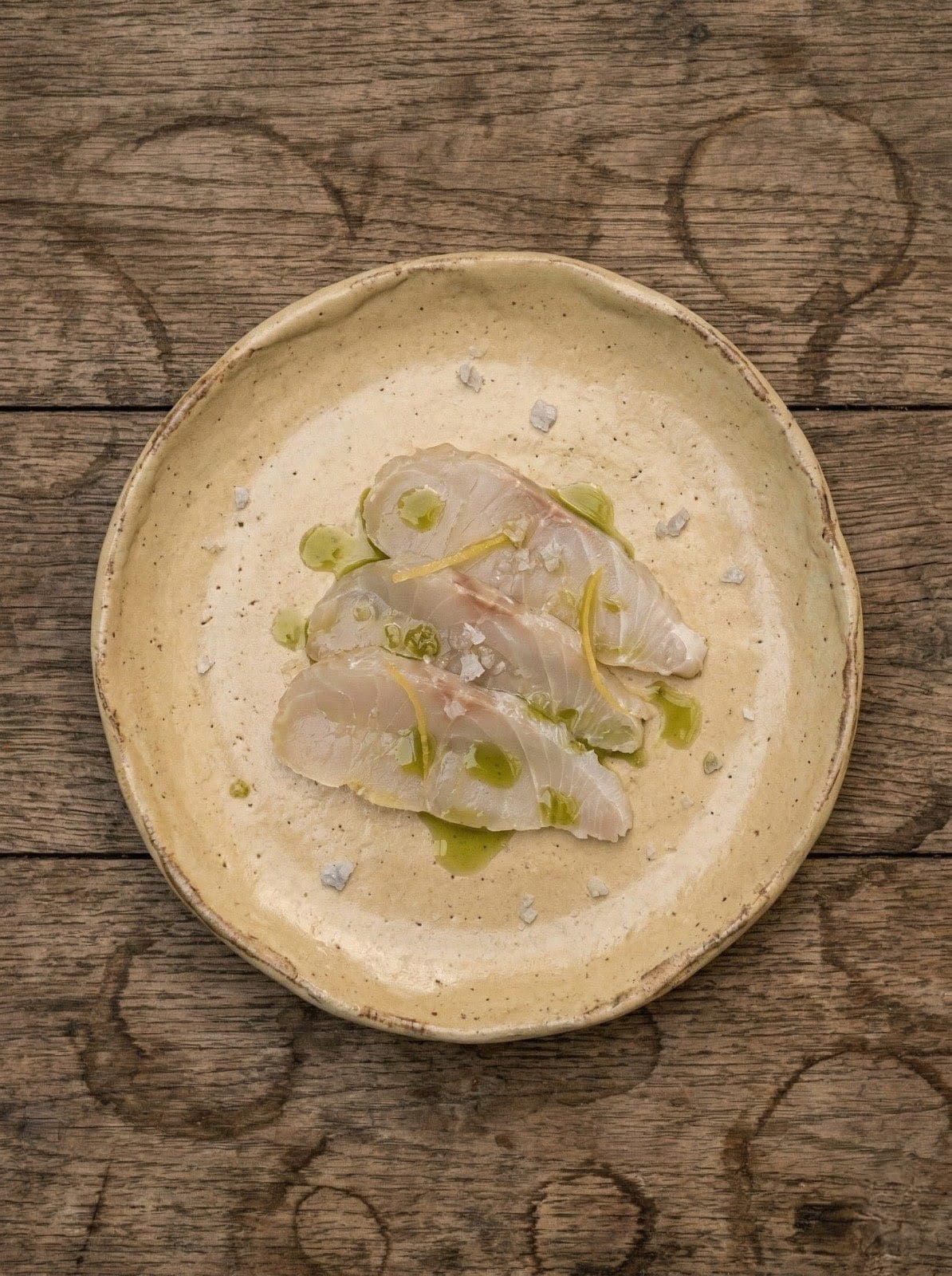 Láminas de corvina curada sobre plato de cerámica ocre